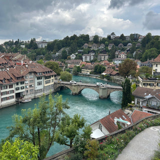 Aerial view of Bern and the turquoise  Aare river running through it, surrounded by greenery and buildings.