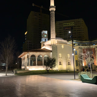 A night time photograph of the clock tower built from pale stone in Skanderbeg Square. Tirana, Albania