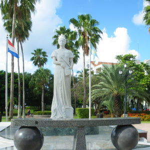 White marble statue of Queen Wilhelmina of the Netherlands, surrounded by a lush waterfront park