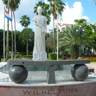 White marble statue of Queen Wilhelmina of the Netherlands, surrounded by a lush waterfront park