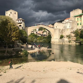 Single span arched stone bridge, Stari Most, in Mostar. The yellow stone glows in the sun despite the dark storm clouds overhead.